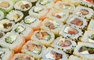 Close-up of a lot of sushi rolls with different fillings lie on a wooden surface. Macro shot of cooked classic Japanese food with a copy space.