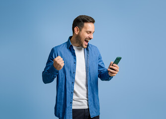 Businessman screaming and pumping fist after receiving good news over cellphone on blue background