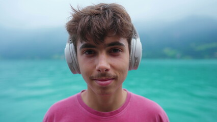 Portrait of young boy putting headphones listening to audio overlooking lake shire landscape....