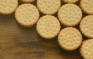 A round sandwich cookie with coconut filling lies in large quantities on a brown wooden surface. Photo of edible treats on a wooden background with copy space