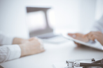 Stethoscope lying on the tablet computer in front of a doctor and patient sitting opposite each other and using tablet computer at the background . Medicine, healthcare concept