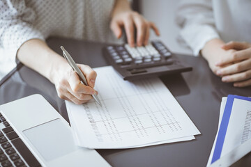 Woman accountant using a calculator and laptop computer while counting taxes for a client. Business audit concepts - 672216988