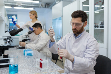 Obraz premium Mature serious and concentrated man works inside the laboratory, scientist conducts experiments examining the microscope.