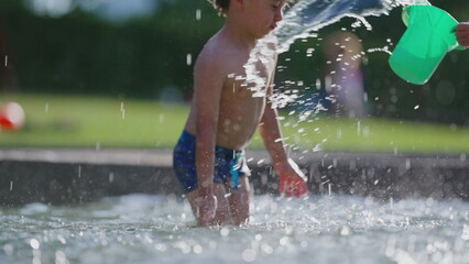 Splashing little boy with bucket of water in 120 fps slow-motion at public swimming pool, hot...