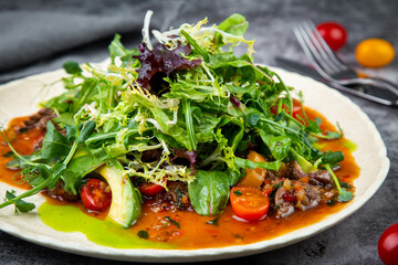 meat gravy with meat, cherry tomatoes and a bunch of greens on top, side view