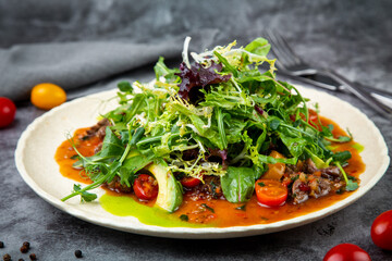 meat gravy with meat, cherry tomatoes and a bunch of greens on top, side view