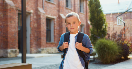 Portrait of little boy with backpack looking to camera standing on the school yard. portrait happy kid child. change school yard. portrait happy student.