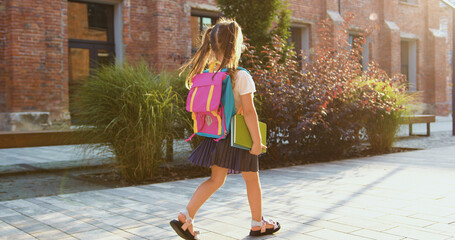 Little girl with backpack and textbook going hurrying to school. Attaractive schoolgirl with a backpack fun runs from school to home.