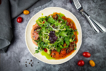 meat gravy with meat, cherry tomatoes and a bunch of greens on top, top view