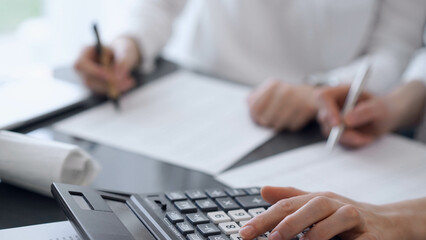 Two accountants use a calculator and laptop computer for counting taxes or revenue balance. Business, audit, and taxes concepts - 672221960