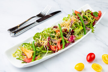 green salad with cherry tomatoes on a white oblong plate, side view