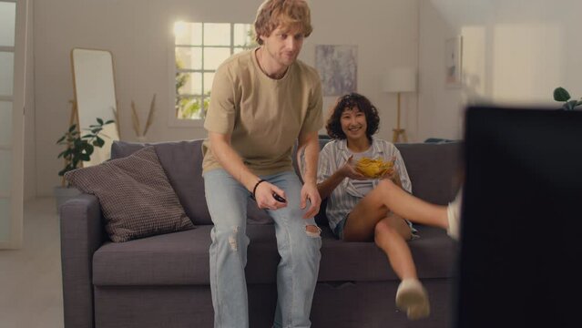 Young married couple coming into living room with bowl of tachos ready to watch movie together