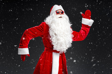 Funny emotional man wearing Santa Claus suit, glasses dancing, having fun on New Year party isolated on black background 