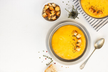 Bowl of pumpkin or vegetarian cream soup decorated with fresh rosemary, olive oil and croutons, on white textured background. Top view, copy space. square image