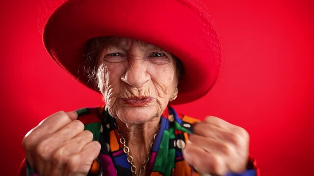 Angry unhappy displeased fisheye portrait caricature of funny elderly woman saying NO with red hat isolated on red background.
