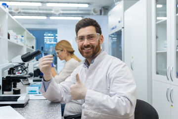Naklejka na ściany i meble Satisfied with research results, scientist lab assistant shows thumbs up to camera, mature experienced lab worker uses microscope inside building