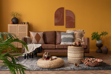 Warm and cozy composition of african living room interior with mock up poster frame, brown sofa,...