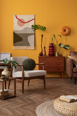 Aesthetic composition of vintage living room interior with kilim rug, wooden sideboard, boucle armchair, glass vase with leaves, yellow wall, round rug and personal accessories. Home decor. Template.