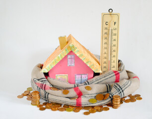 Model home with a scarf, stacks of money and thermometer.Rising heating costs, inflation,Thermal...