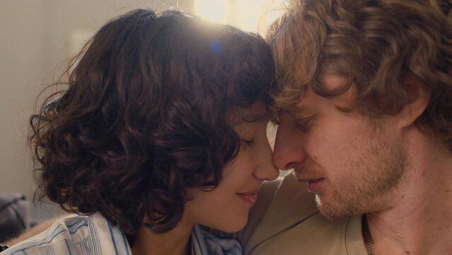 Close-up shot of young happy married couple leaning their heads to each other smiling and gently talking with one another