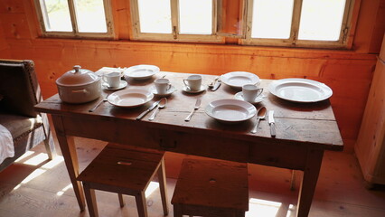 Classic ceramic tableware in pastoral setting. White plates, teacups, and utensils displayed on old wooden table