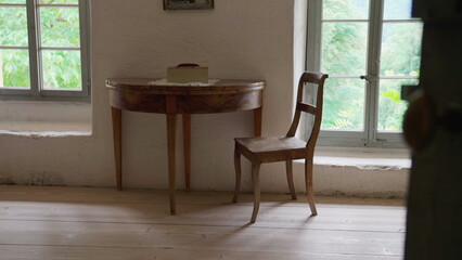 Rustic farmhouse setting, antique wooden table and chair by window in rural house