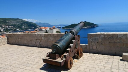 Fototapeta na wymiar Old cannon on the fortress Lovrijenac with the old town of Dubrovnik and the island of Lokrum