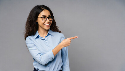 Happy young smiling professional business woman wearing blue shirt looking at camera pointing finger away at copy space showing aside presenting advertising offer standing isolated at gray background