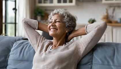 Smiling relaxed mature old woman resting dreaming sitting on couch at home