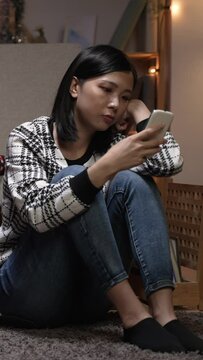 Vertical Screen: annoyed chinese girlfriend while she is complaining and playing with phone on floor in the living room at home