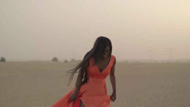 Swarthy young woman with long hair walking barefoot on desert sand in a dress developing in the wind