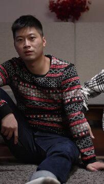 Vertical Screen: unhappy asian married couple pushing each other while they are sitting on the ground watching tv and using phone after a fight in the living room at home