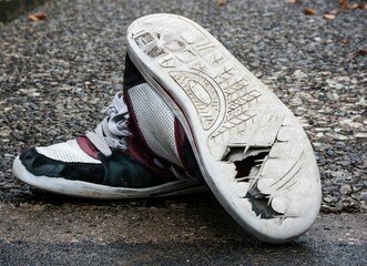 Pair of aged and worn sneakers on the pavement.