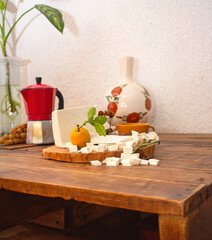 Queso frescoes en cubos sobre una mesa en una cocina con un florero y cafetera representación de lo casero y natural en preparación de alimentos