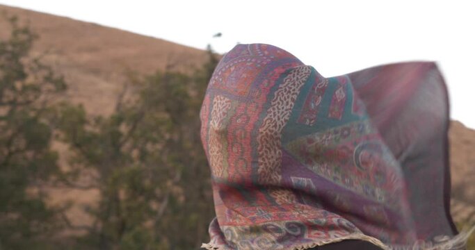Close-up portrait of a lonely woman with a scarf on her face. The wind tries to blow away the scarf and free the personality. Visual display of psychological state