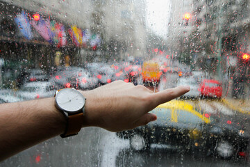 A man's hand is pointing outward from the window with raindrops. He has a modern and elegant watch...