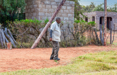 old african man walking on a dirt road in the village, smoking a pipe