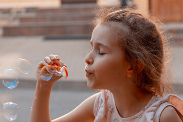 A little girl with red or brown hair blows soap bubbles. The concept of a carefree, happy, peaceful...
