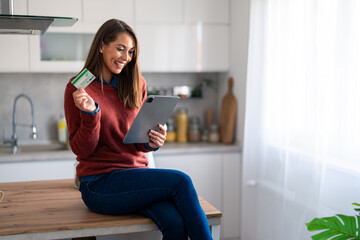 Smiling young adult woman holding credit card while shopping online over digital tablet pc.