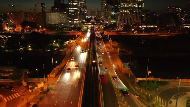 Forwards tracking of subway train driving on tracks in center of multilane road in modern urban district. Skyscrapers in La Defense at night. Paris, France