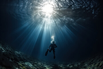 In this captivating underwater photograph, the silhouette of a lone diver is suspended in the deep blue sea. The rays of the sun penetrate the surface, creating a stunning display of light that reache