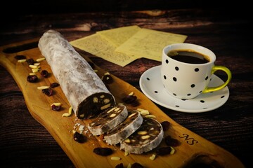 Closeup of a chocolate roll with cookies on a wooden board, served with a cup of coffee