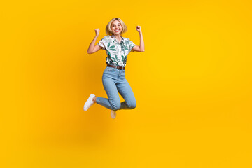 Full length photo of overjoyed lucky cute girl dressed print shirt win bet clenching fists jumping isolated on yellow color background