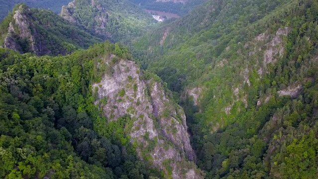 Aerial Drone flight above rocky mountain peaks covered with luxuriant and wild beech forests. The valley winds through sharp ravines. Olt river flows in the background. Carpathia, Romania.