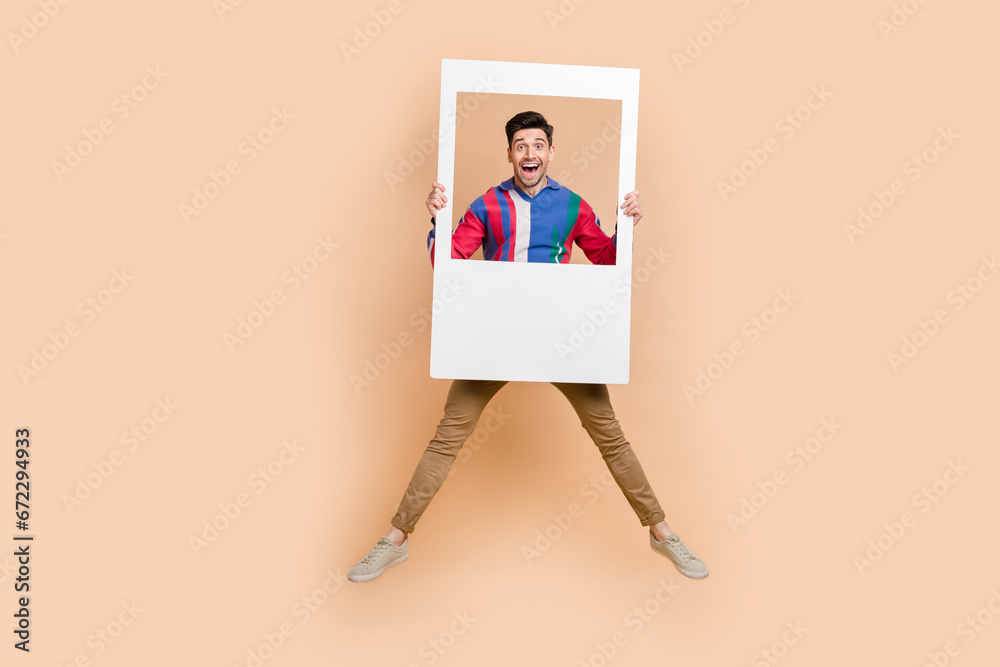 Sticker Full body photo of jumping crazy guy have fun holding huge paper zone for portrait cadre snapshot isolated on beige color background