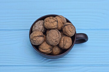 a bunch of walnuts in a brown ceramic cup stands on a blue wooden table