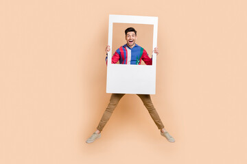 Full body photo of jumping crazy guy have fun holding huge paper zone for portrait cadre snapshot isolated on beige color background