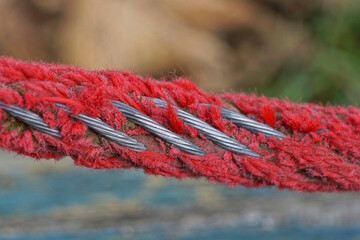 part of a gray steel cable in a red shabby winding on the street - Powered by Adobe