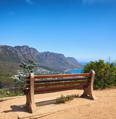 Bench with a beautiful view of the mountain and sea against a clear blue sky background with copy space. Relaxing spot for a peaceful break to enjoy the scenic landscape after a hike up a cliff - obrazy, fototapety, plakaty