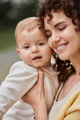 portrait of smiling woman with closed eyes embracing toddler child outdoors, happy moments
